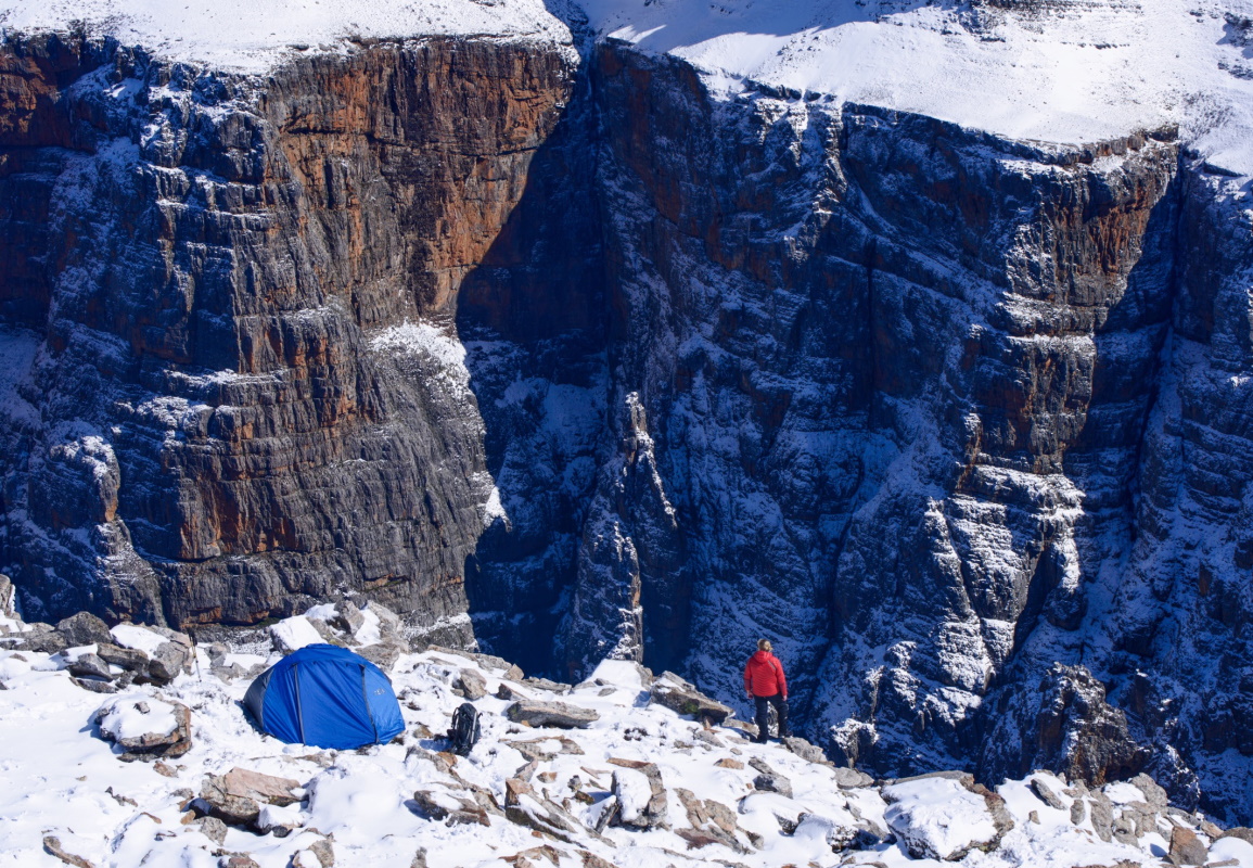 One person standing on the edge of a cliff with a First Ascent Tent